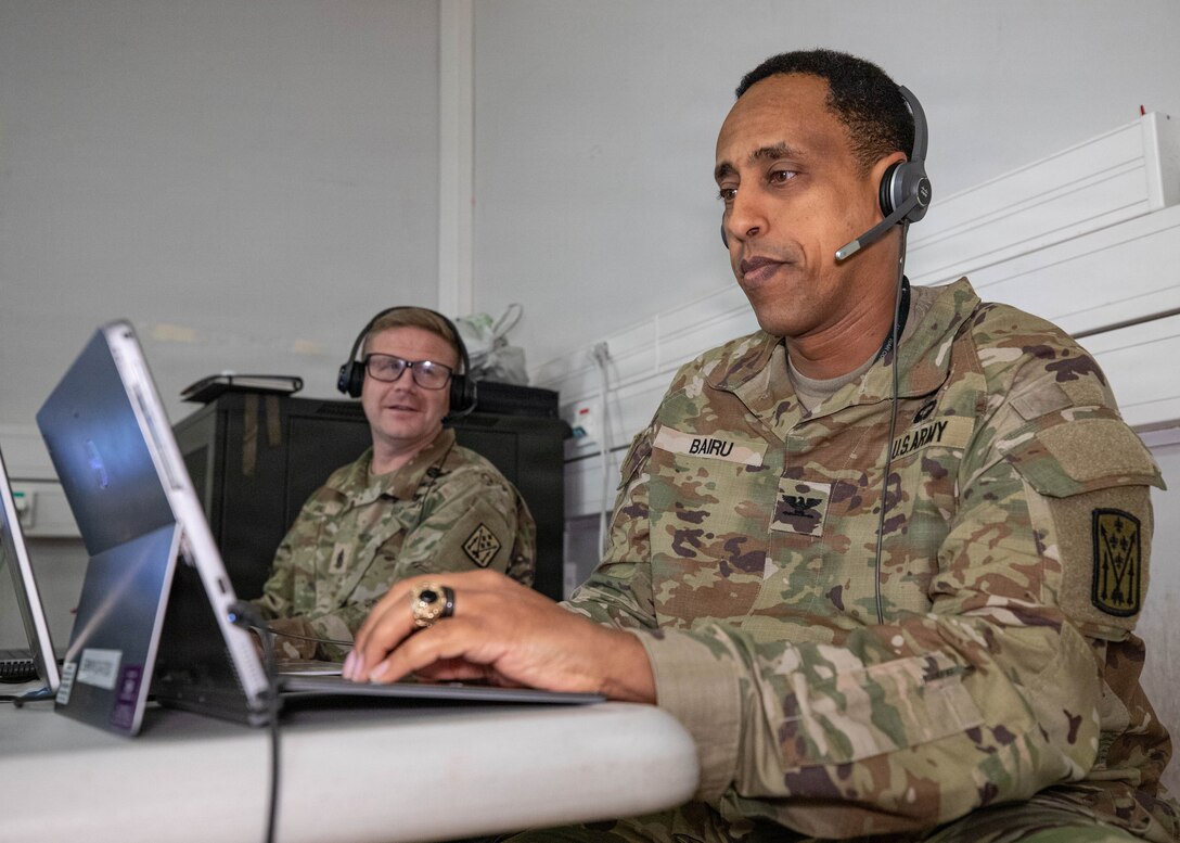 U.S. Army Col. Haileyesus Bairu, Commander of the 52nd Air Defense Artillery Brigade, listens to a Fires Support Element update brief in support of simulated V Corps operations with senior enlisted leader Paul Kenneth, left, Command Sgt. Maj. of the 52nd Air Defense Artillery Brigade, during Avenger Triad 25, Oct. 30, 2025, Camp Kosciuszko, Poland.