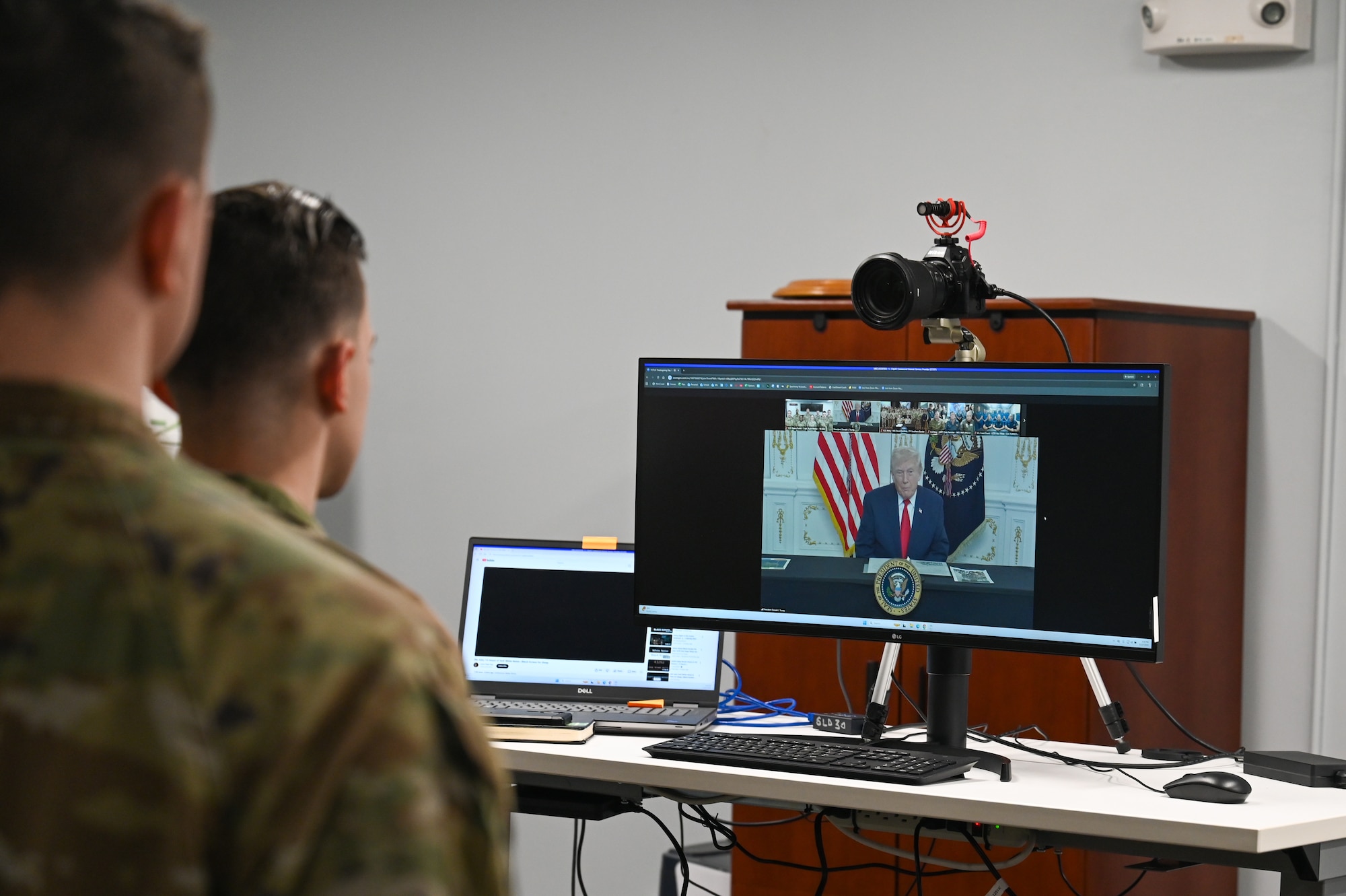 Two service members watch U.S. President Donald J. Trump express his gratitude to the team for their dedication on a virtual call.