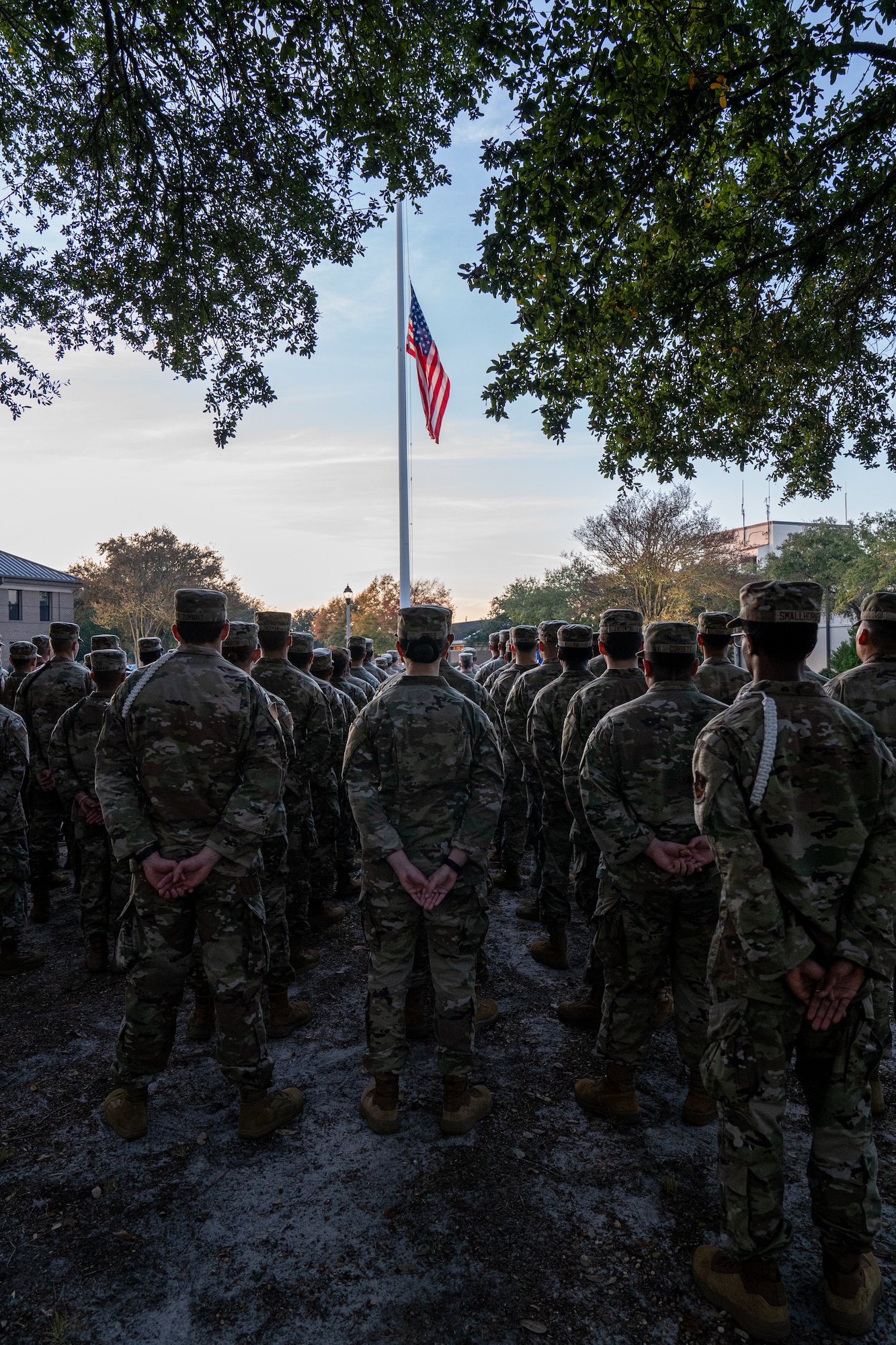 Service members wearing OCPs in a flight formation stand behind a flag pole.