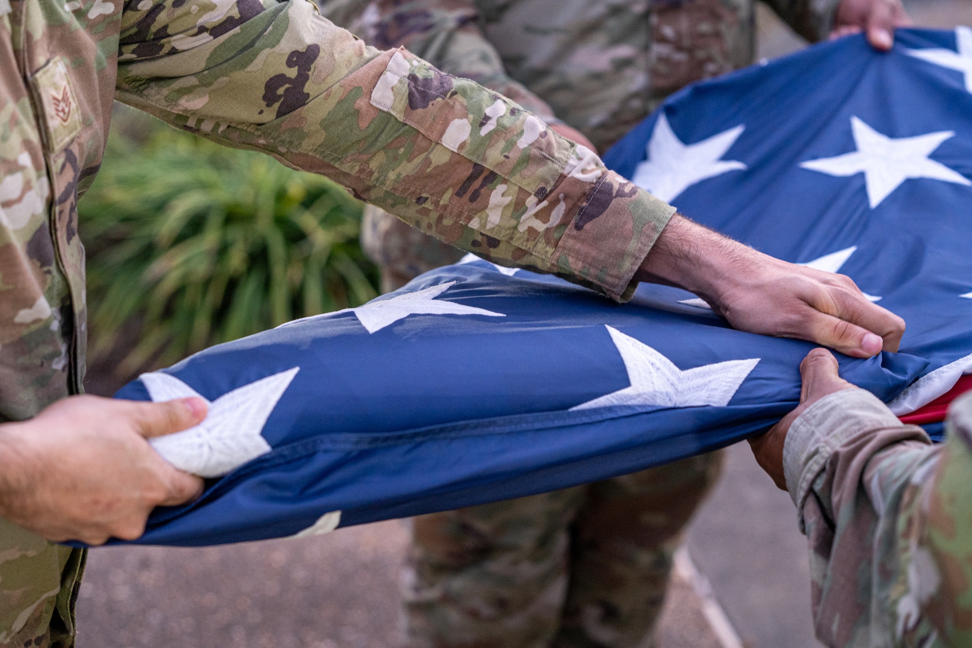 Hands tightening a folded flag while other hands hold it in place.