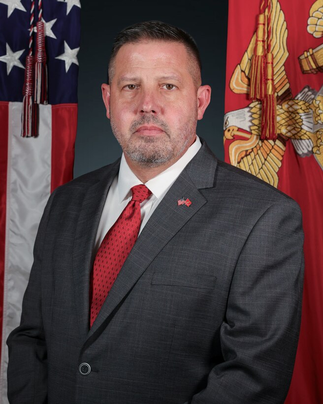 A photo of Jeffery M. Morgan, chief of staff of Marine Corps Recruiting Command taken on Marine Corps Base Quantico, Sept. 30, 2025. A man in a suit stands in front of the american flag and the marine corps flag.