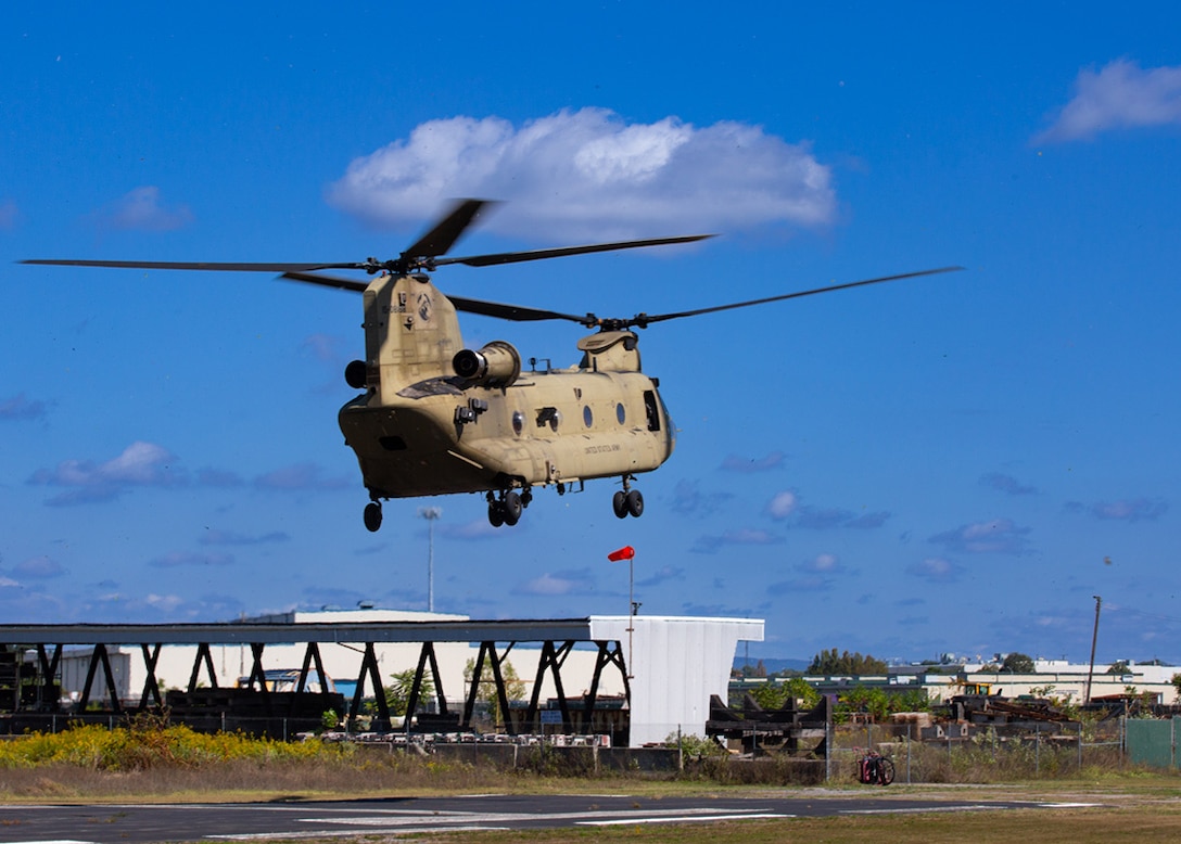 A Chinook helicopter hovers above the ground with blue skis behind it.