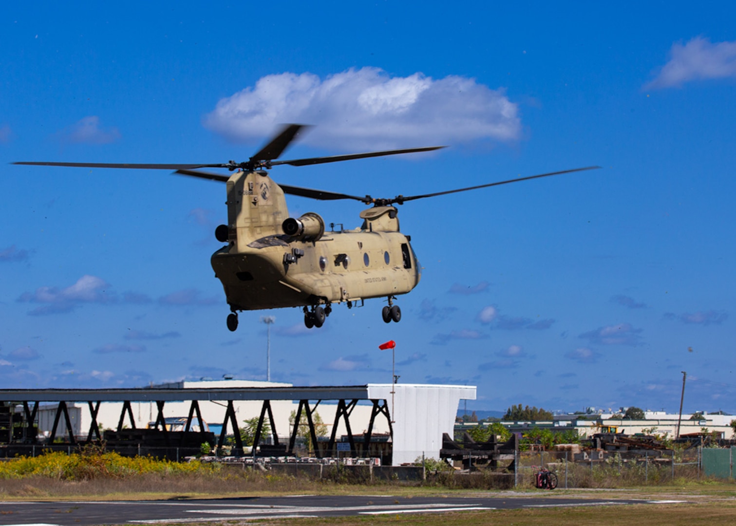 A Chinook helicopter hovers above the ground with blue skis behind it.