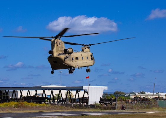 A Chinook helicopter hovers above the ground with blue skis behind it.
