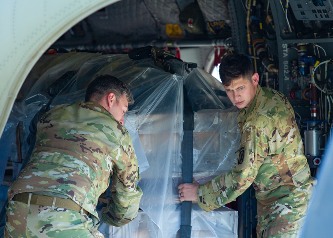 Two Soldiers move a large container inside a helicopter.