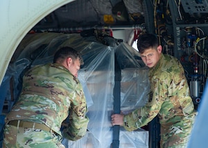 Two Soldiers move a large container inside a helicopter.