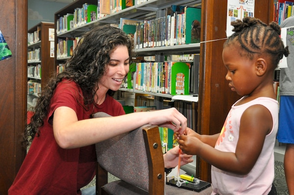 KINGS BAY, GEORGIA (June 28, 2024) Evelyn Ashe, Strategic Weapons Facility, Atlantic (SWFLANT) engineering student intern, helps a child prepare her straw missile for launch at the Camden County Public Library in Kingsland, Georgia, June 28, 2024. A team of volunteers from SWFLANT, Lockheed Martin and General Dynamics hosted the event during the Science, Technology, Engineering, and Mathematics (STEM) day of the library’s summer learning series. (U.S. Navy photo by Ashley Berumen)