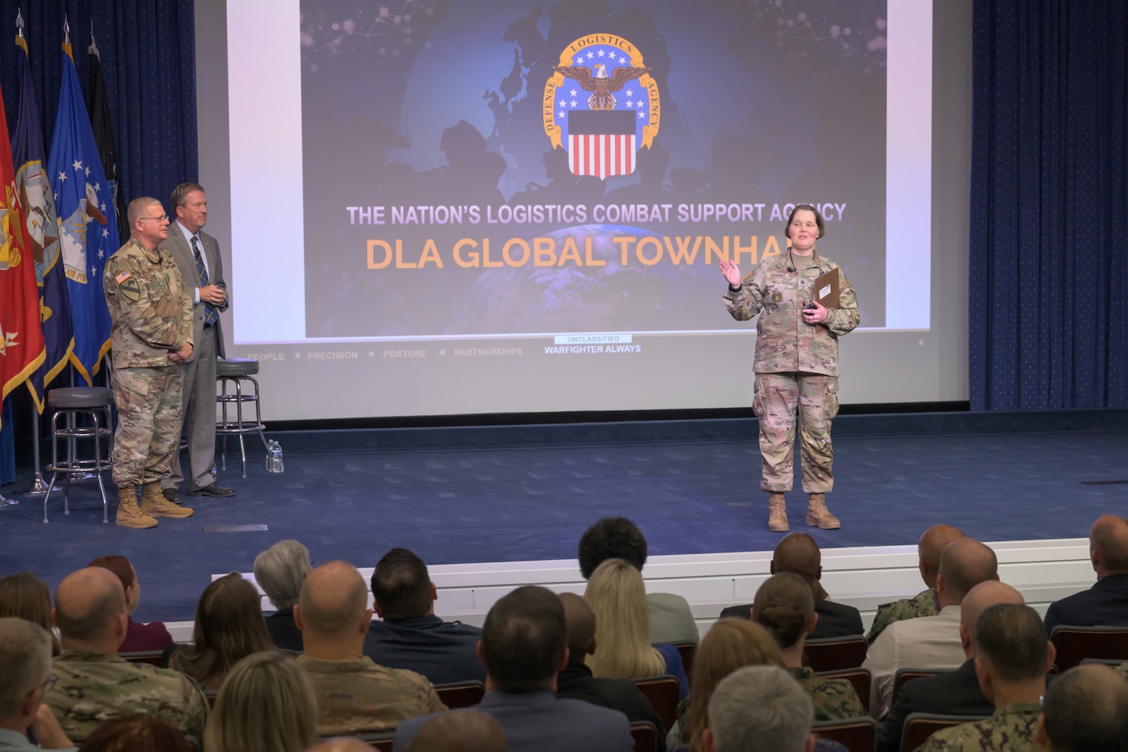An Army Command Sergeant Major is in uniform on a stage speaking to an audience.