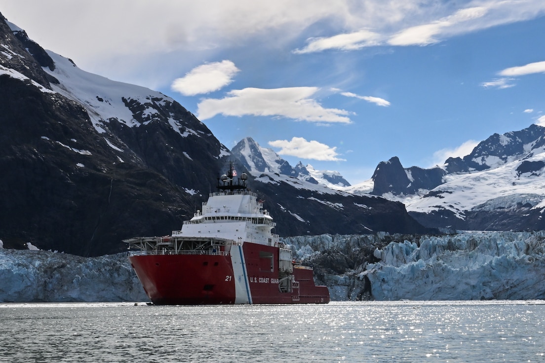 Image of U.S. Coast Guard Cutter Storis transiting icy waters with mountains in the background.