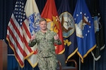 A Navy rear admiral talks on a stage in an auditorium.