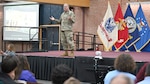 A military general stands on a stage speaking to an audience