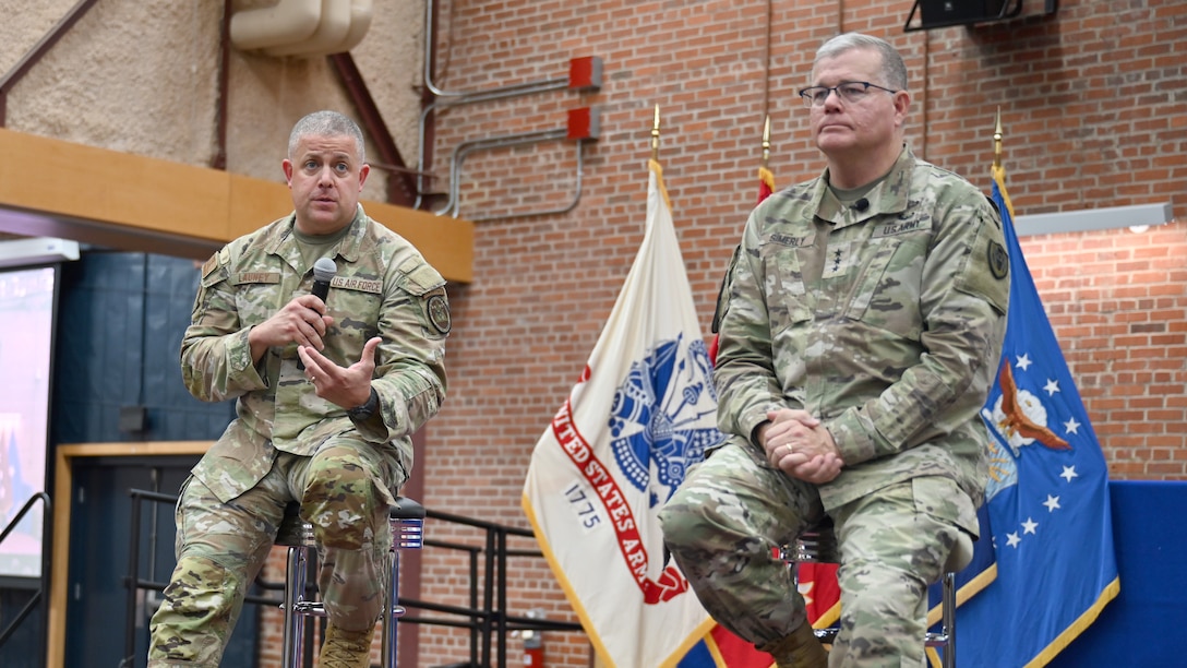 Two military men set on stools on a stage