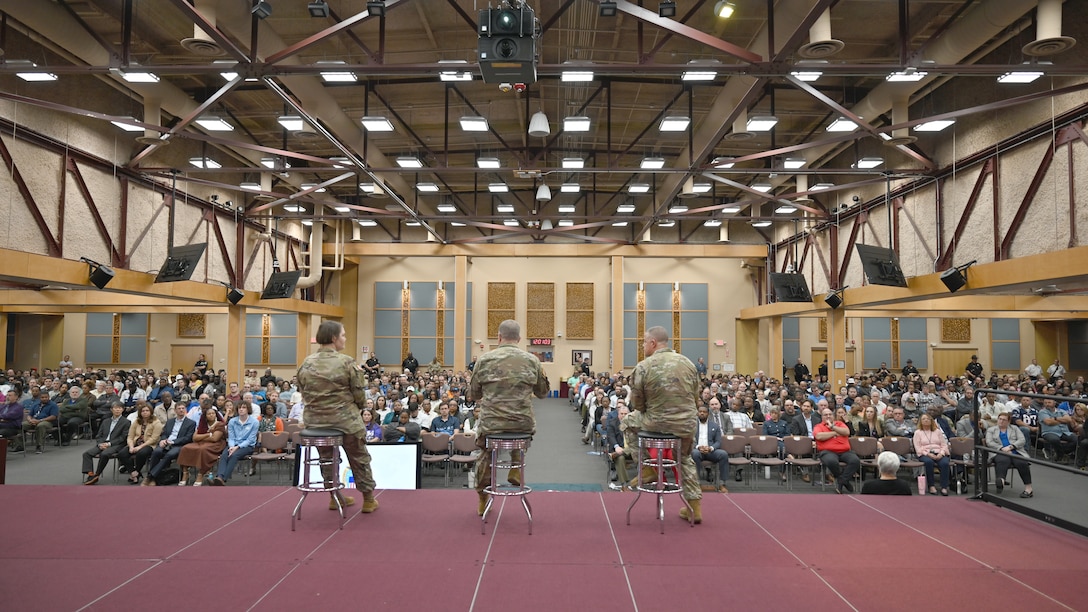 Three military members are on a stage looking at an audience