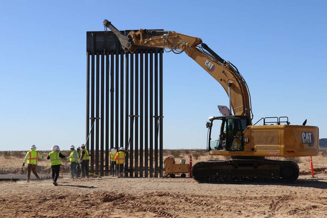 A steel panel is put into place via a modified excavator along the U.S. southern border.