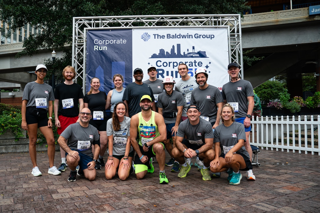 15 racers pose for a group phot in front of the Corporate Run race Banner.