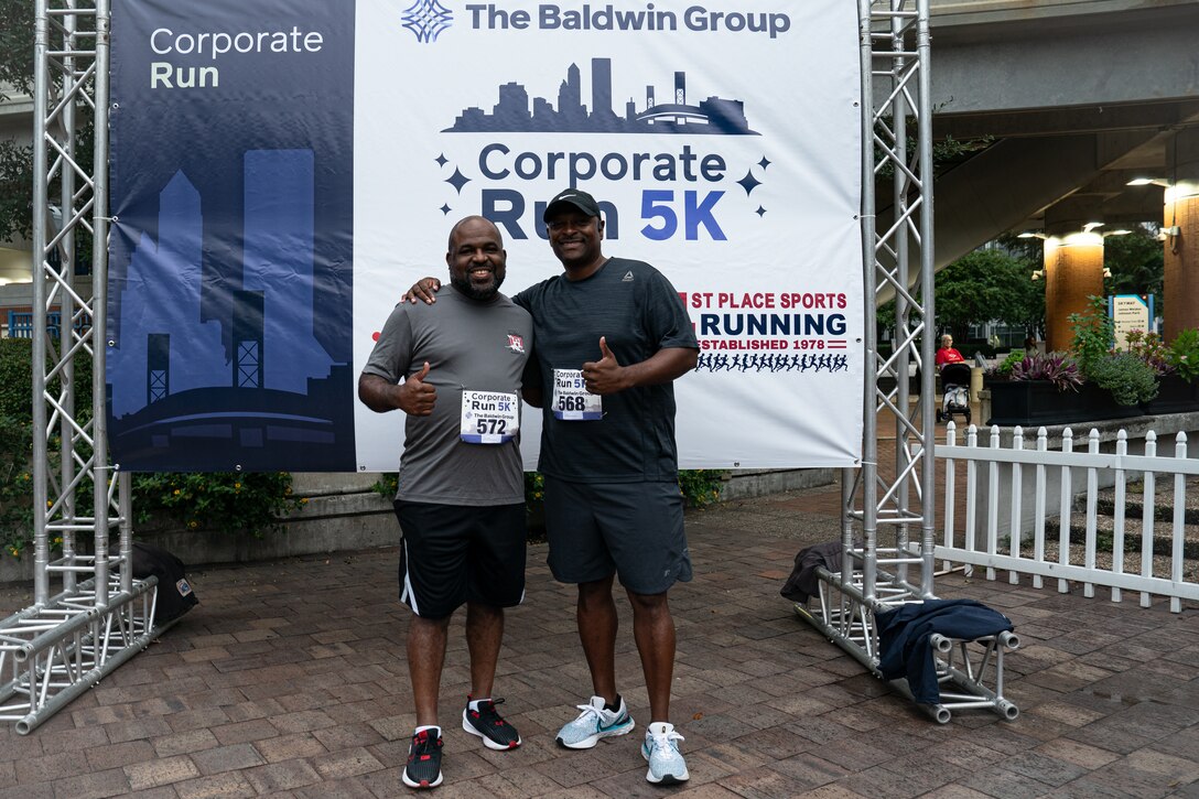 two runners pose in front of the race day banner