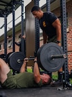 U.S. Marine Corps Staff Sgt. Donald Baker, a force fitness instructor trainer with Training Command, spots a student with the National Capital Regions Staff Sergeant Transition Symposium during a floor bench press while conducting a physical training event at Butler Stadium on Marine Corps Base Quantico, Virginia, Aug. 6, 2025. The Fiscal Year 25 NCR Staff Sergeant Transition Symposium is a five-day dynamic professional military education course comprised of FY25 Staff Sergeant selectees from diverse Military Occupational Specialty backgrounds and commands, aiming to shape Marines into ethical, operationally grounded SNCOs. (U.S. Marine Corps photo by Lance Cpl. Braydon Rogers)