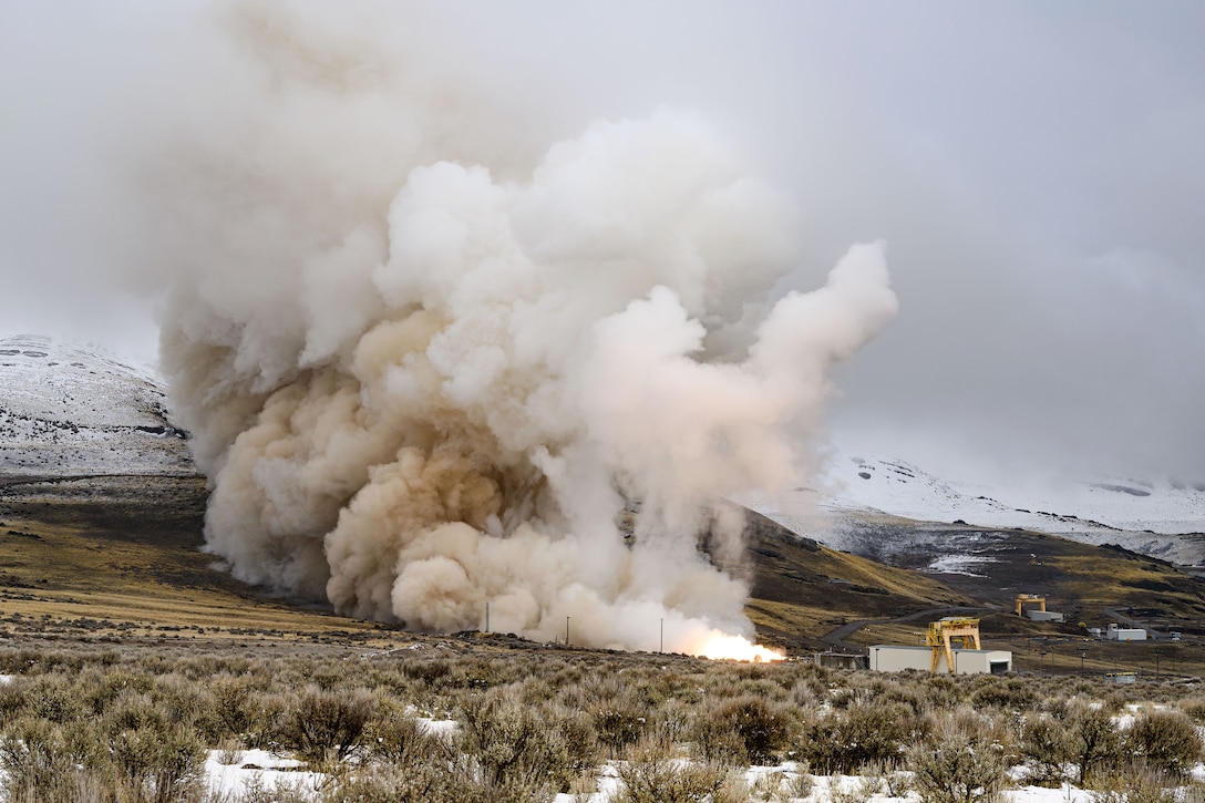 Smoke billows up from a flames shooting from a rectangular device sitting in a hilly, snowy area.