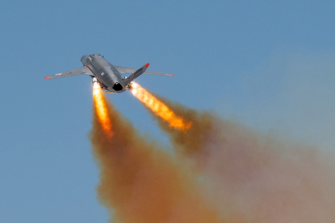 Two flames shoot from an unmanned aircraft ascending in blue sky.