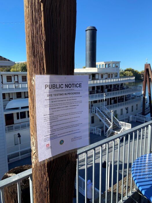 A public notice is posted on a wooden column with a riverboat in the background.