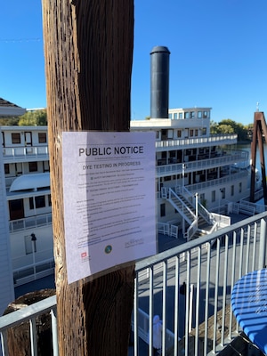 A public notice is posted on a wooden column with a riverboat in the background.