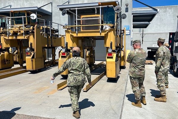 A group of people wearing camouflage military uniforms stand outside looking at large machinery.
