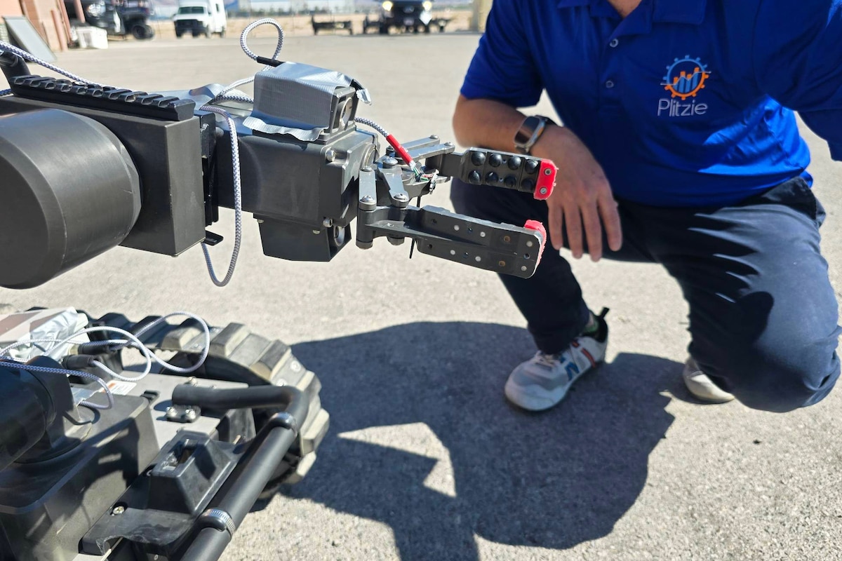 A person dressed in civilian attire kneels in front of a robotic system.