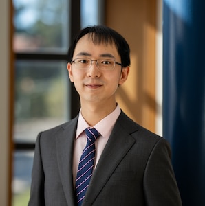 Elliot Ji poses for his headshot, wearing glasses, a suit, and tie.