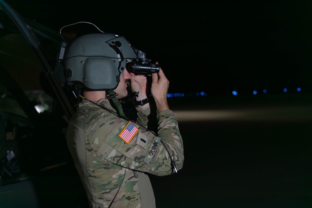 A soldier wearing a helmet adjusts night goggles while outside in the dark.