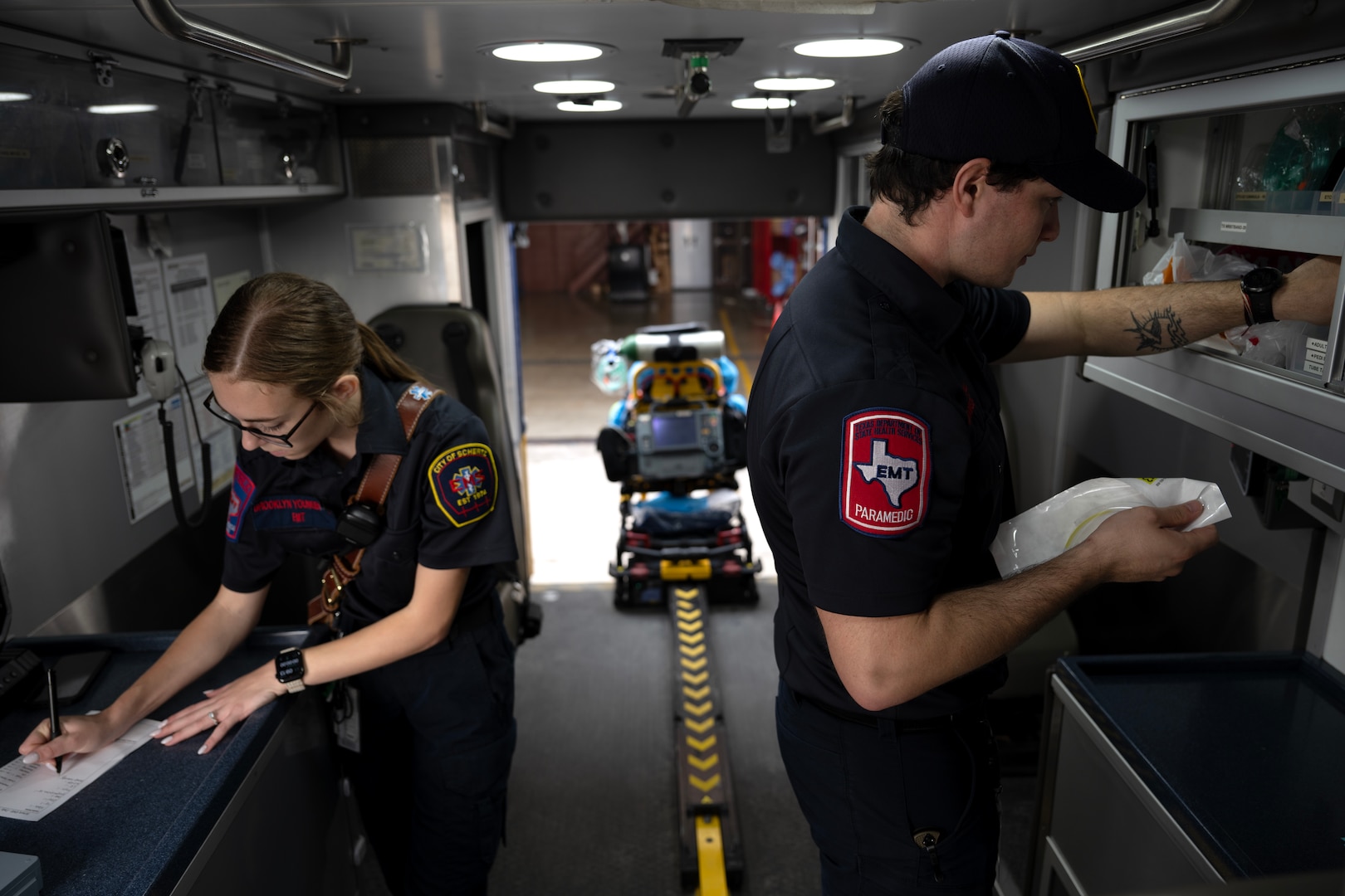 Photo shows two EMS workers inside of the ambulance filling out paperwork and checking on supplies.