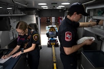 Photo shows two EMS workers inside of the ambulance filling out paperwork and checking on supplies.