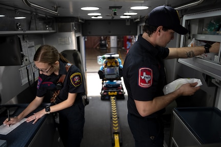 Photo shows two EMS workers inside of the ambulance filling out paperwork and checking on supplies.