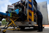 EMS worker stands next to the ambulance as patient is loaded onto the stretcher. Another EMS personnel loads patient onto stretcher.