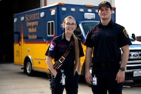 Two EMS, one female and one male, stand in front of an ambulance and pose for the camera.