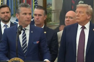 A man in business attire speaks into a microphone from behind a podium while standing next to another man in business attire. Four other men, also in business attire, stand behind them.