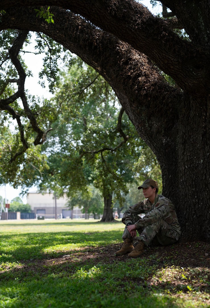 A woman in uniform sits against a tree trunk.