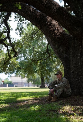 A woman in uniform sits against a tree trunk.
