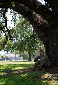 A woman in uniform sits against a tree trunk.