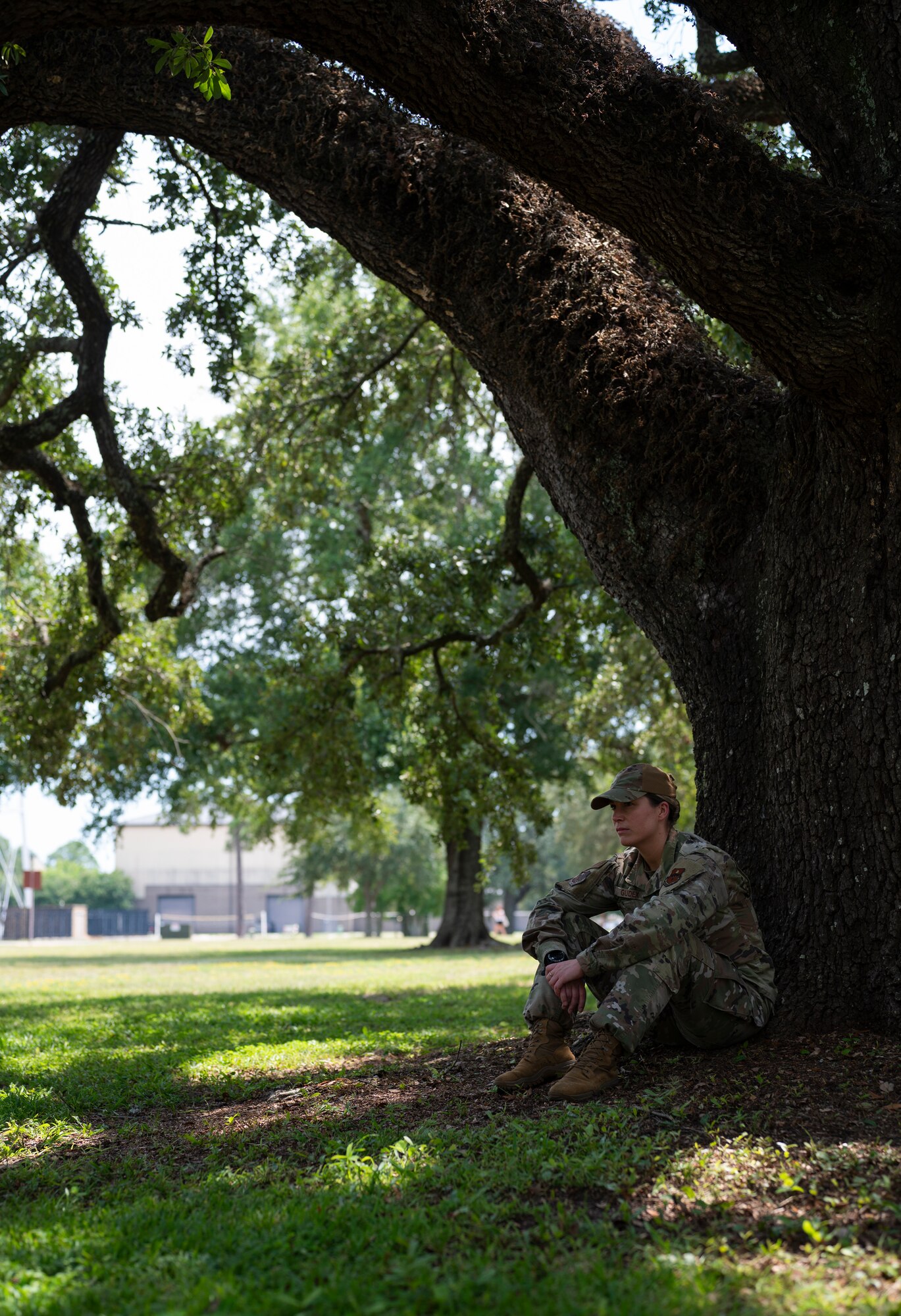 A woman in uniform sits against a tree trunk.