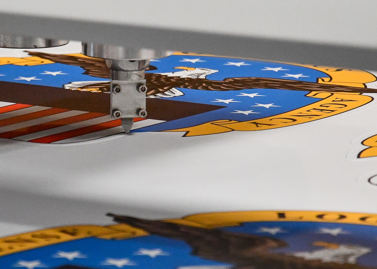A cutting tool cuts next to art work printed on a white sheet of foam board.