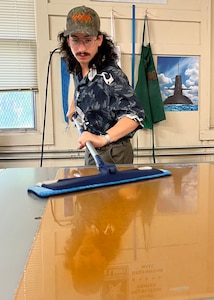 A man cleans the surface of a clear shinny surface. He is using a long handled Swiffer style clearing tool.