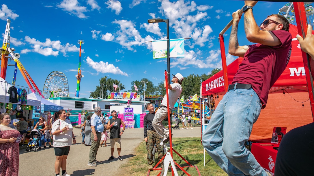 Attendees attempts to do the pull up challenge during the Western Idaho State Fair in Boise, Idaho, Aug. 22, 2025. The Western Idaho State Fair is the biggest State fair in Idaho bringing in over 250,000 attendees. The Marines utilized the Marine pull-up bar challenge to engage with event attendees and talk to them about Marine Corps career opportunities. (U.S. Marine Corps Photo by Lance Cpl. Abram Maestre)