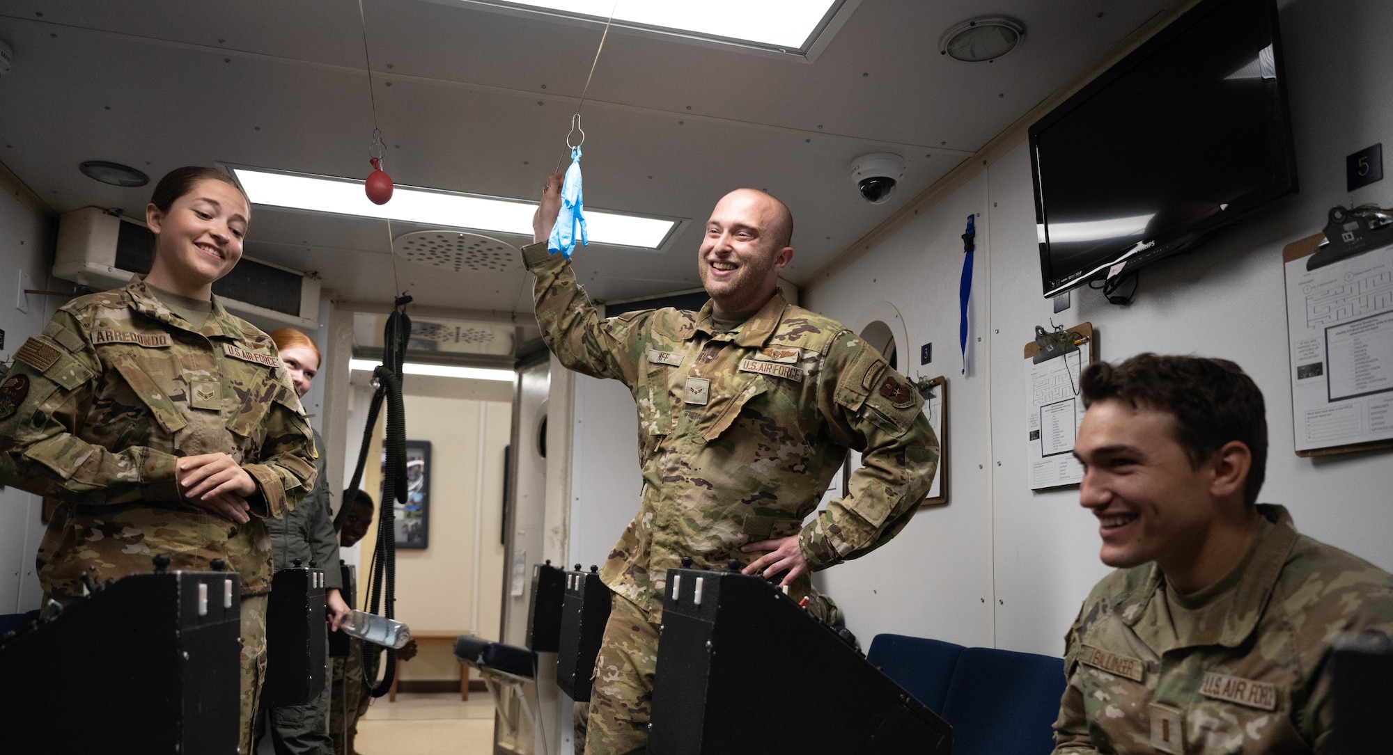 U.S. Air Force Airman 1st Class  Crystal Arredondo, 47th Operations Support Squadron aerospace physiology technician, and Airman 1st Class Cain Paff, 47th OSS aerospace physiology technician, educate 2nd Lt. Cort Ballinger, 47th Student Squadron pilot trainee, about the Hyperbaric Chamber at Laughlin Air Force Base, Texas, Aug. 22, 2025.  The Hyperbaric Chamber tests pilots' symptoms of hypoxia so they can take measures to correct it. (U.S. Air Force photo by Airman 1st Class Darryl Keith.)