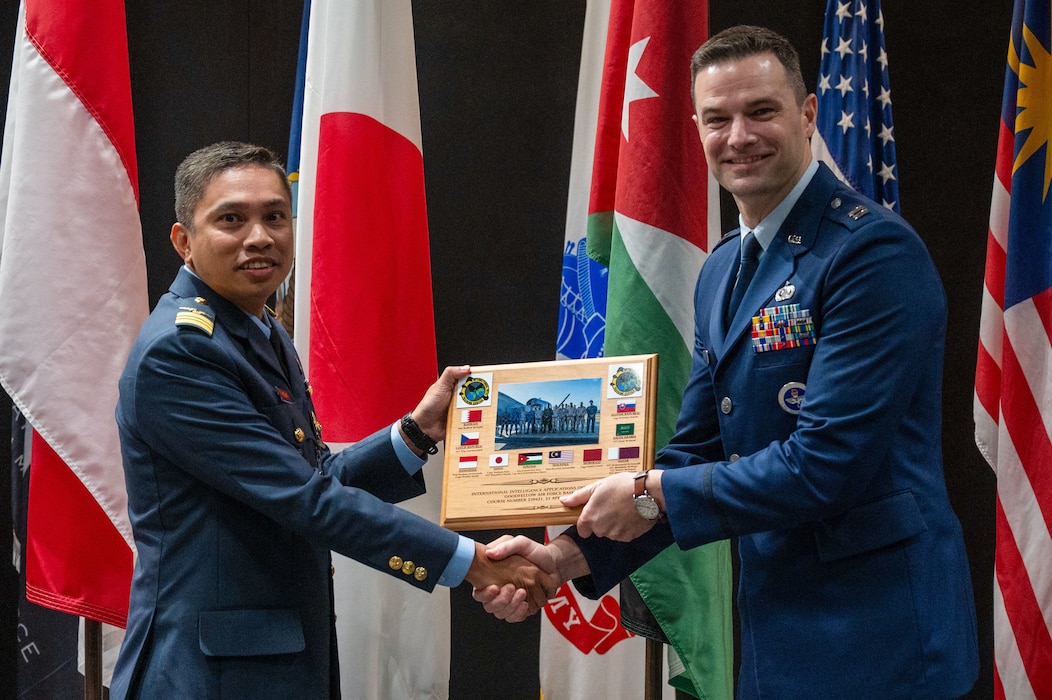 Royal Malaysian Air Force Maj. Rozaimi Bin Jamaludin, a student in the International Intelligence Applications Officer Course, presents U.S. Air Force Capt. Ryan Best, International Intelligence Training Center flight commander, with a plaque on behalf of the class at the Powell Event Center, Goodfellow Air Force Base, Texas, July 18, 2025. This iteration of the course included officers from 10 different countries, representing a diverse coalition of global military partners. (U.S. Air Force photo by Airman 1st Class James Salellas)