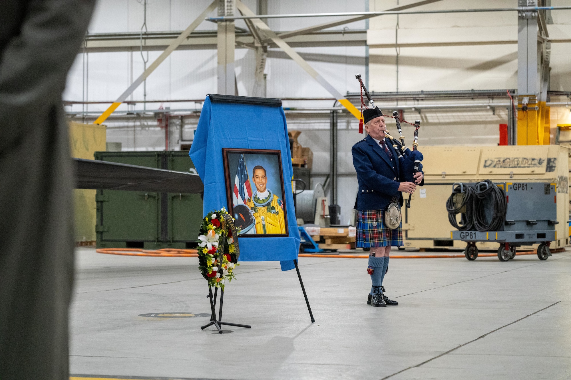 A bagpiper performs beside a portrait of Capt. David “Hawk” Hawkens