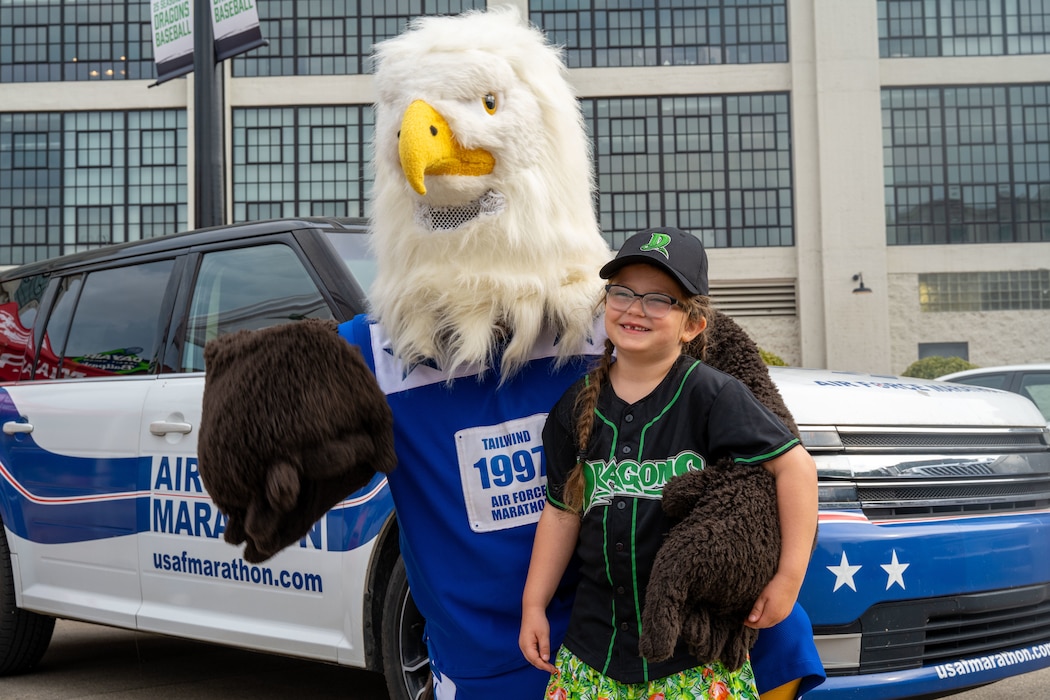 An attendee at the Dayton Dragons American Celebration Night poses for a photo with Air Force Marathon Mascot Tailwind during the pregame activities outside Dayton Air Ballpark, Aug. 23, 2025. In addition to throwing out the pitch, 30 individuals took the oath of enlistment to delayed enlistment personnel during the game. (U.S. Air Force photo by Jack Gardner)