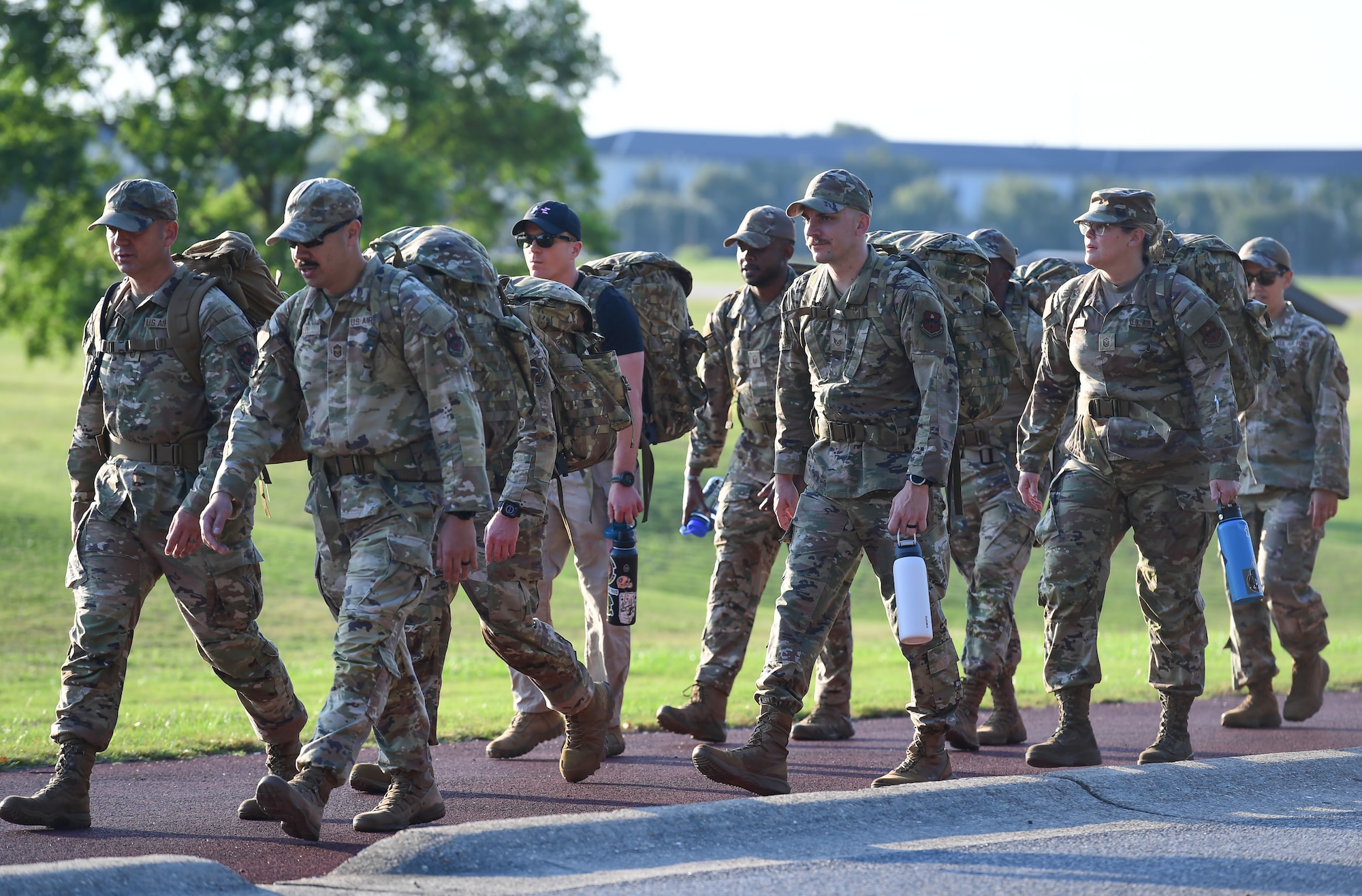 A group of people march while carrying ruck sacks on their backs.