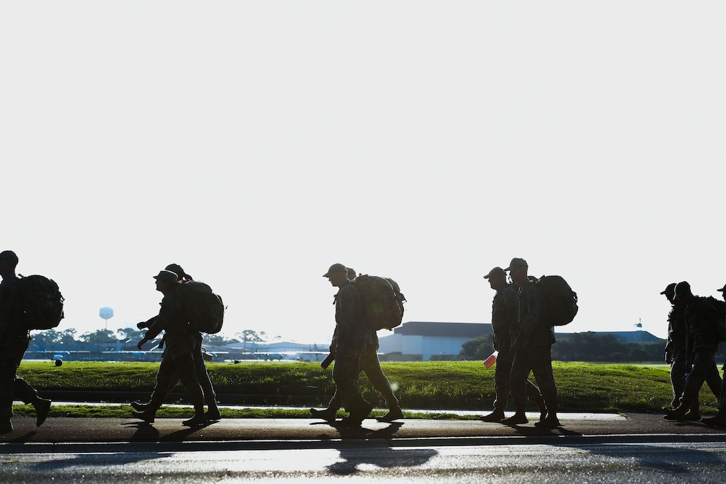 A group of people walk in formation while carrying ruck sacks.
