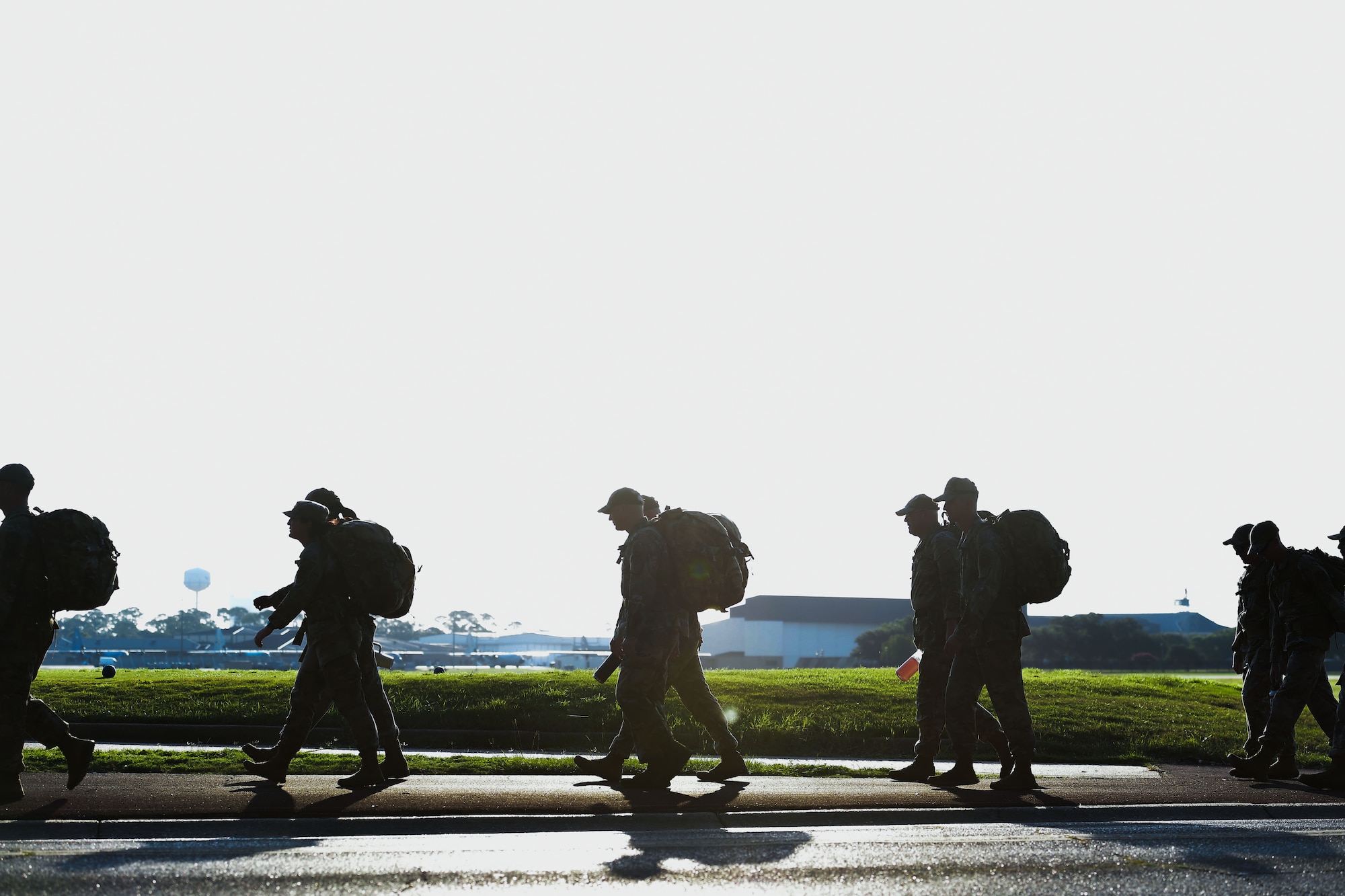 A group of people walk in formation while carrying ruck sacks.