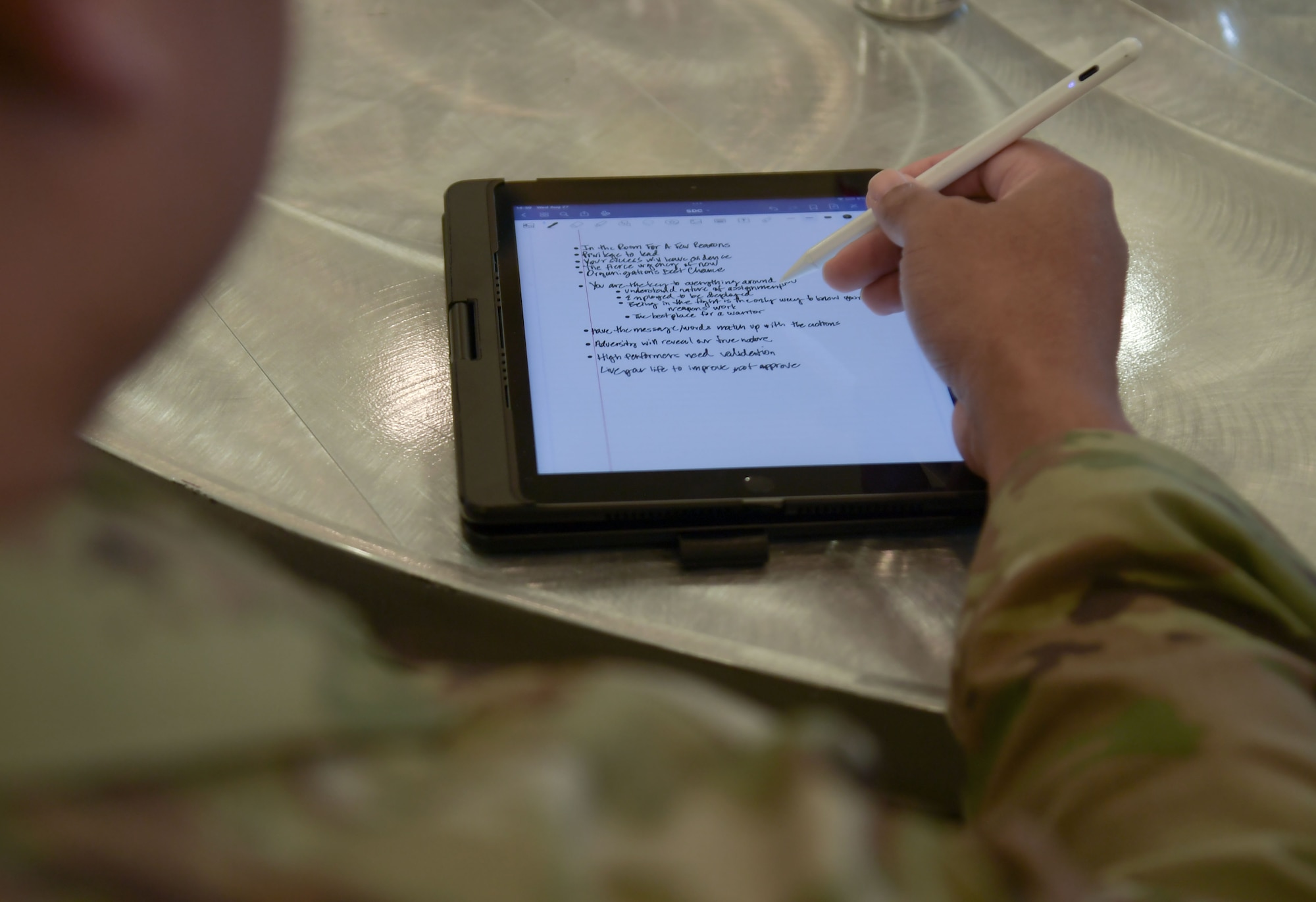 A man in military uniform writes notes in a tablet.